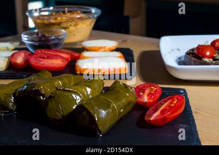 Dolma, deliziosa cucina casucasiana e turca, foglie di vite farcite con carne tritata e riso. Crema di hummus tradizionale e formaggio in background. Foto Stock