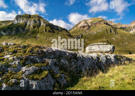 Suggestivo paesaggio montano, cielo blu con nuvole bianche, pendii erbosi con pareti di roccia di dolomite rosa. Piani eterni, Parco Nazionale Dolomiti Bellunesi Foto Stock