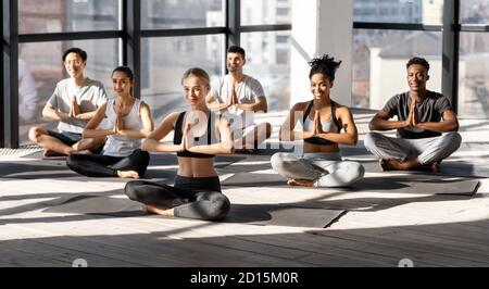 Formazione di gruppo. Persone multietniche sportive che meditano insieme in studio moderno, praticando yoga Foto Stock