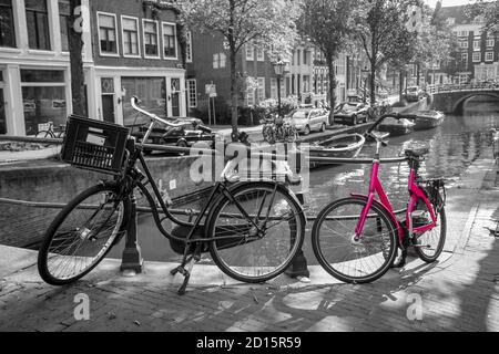 Una foto di una bici rosa sul ponte sul canale di Amsterdam. Lo sfondo è bianco e nero. Foto Stock