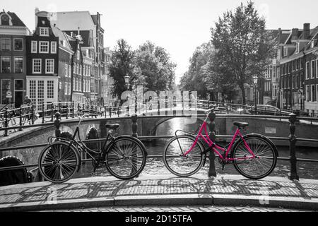 Una foto di una bici rosa sul ponte sul canale di Amsterdam. Lo sfondo è bianco e nero. Foto Stock