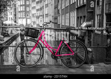 Una foto di una bici rosa sul ponte sul canale di Amsterdam. Lo sfondo è bianco e nero. Foto Stock