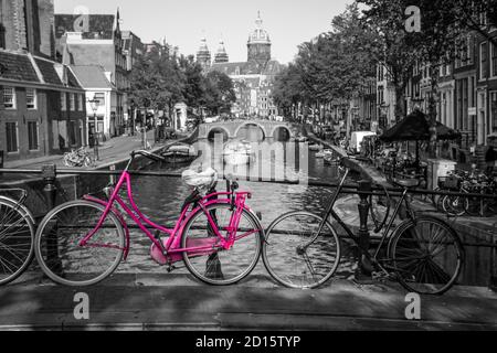 Una foto di una bici rosa sul ponte sul canale di Amsterdam. Lo sfondo è bianco e nero. Foto Stock