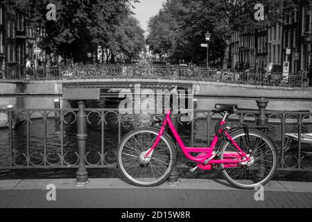 Una foto di una bici rosa sul ponte sul canale di Amsterdam. Lo sfondo è bianco e nero. Foto Stock