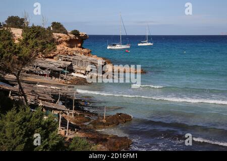 Spagna, Isole Baleari, formentera, Cala Saona, boathouses di fronte a barche a vela ancorate in acque turchesi Foto Stock