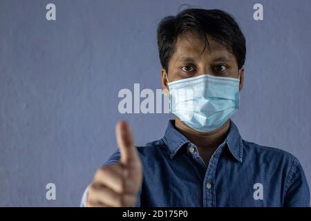 Indiano uomo che indossa monouso chirurgico o medico covid19 influenza influenza maschera di protezione che mostra il pollice in su come un gesto Foto Stock