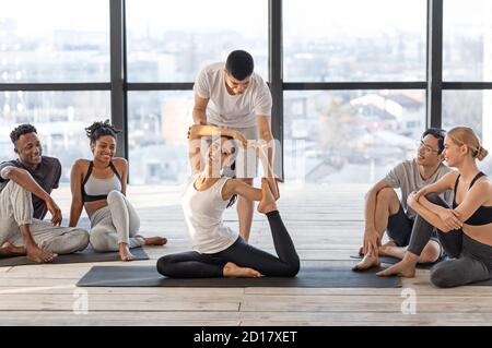 Istruttore professionale di yoga che aiuta i membri del gruppo in asana difficile, correggendo la postura Foto Stock