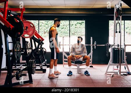 due uomini che indossano maschere di faccia parlano mentre si lavora a. la palestra Foto Stock
