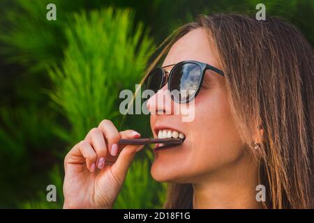 Carina giovane femmina mangiare cioccolato bar. Primo piano di donna faccia mordere cioccolato fondente. Foto Stock