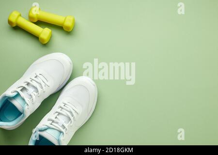 Creativo piatto di attrezzature sportive e fitness. Sneaker bianche e manubri verdi da donna su sfondo verde chiaro. Foto Stock