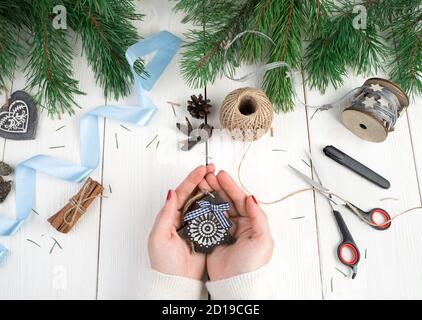 Albero di Natale in legno nelle mani di una donna su sfondo di nastro blu, fili, rami di abete. Foto Stock