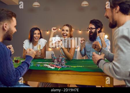 Donna eccitata che mostra 2 assi seduti al tavolo da poker con amici felici alla festa a tema del casinò Foto Stock