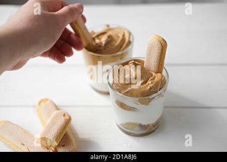 Tiramisù al caffè Dalgona ghiacciato, dessert al caffè alla moda morbido e cremoso. La donna prende la panna montata con il biscotto. Tiramisù con bevanda coreana. Dessert espresso latte con schiuma di caffè. Foto Stock