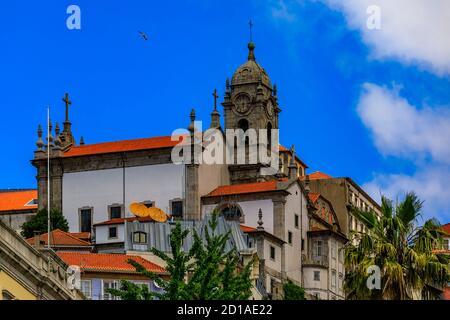 Facciate e tetti in tegole rosse di tradizionali case portoghesi nel centro storico con una torre in pietra sullo sfondo a Porto, Portogallo Foto Stock