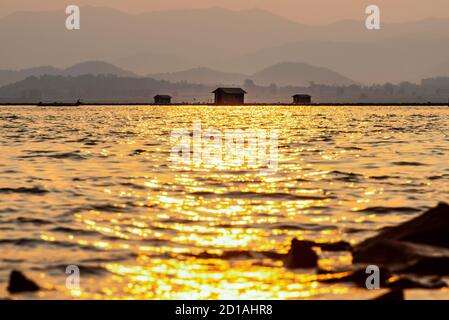 Bella natura paesaggio silhouette pescatore e gabbie di allevamento di pesce, luce del sole dorata che si riflette sulla superficie dell'acqua al tramonto, pesca locale rurale Foto Stock