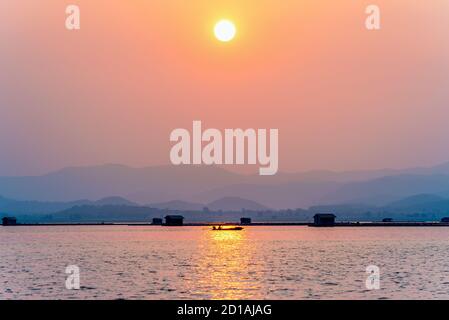 Bella natura paesaggio silhouette pescatore guida una barca a casa sotto il sole, luce dorata sul cielo rosso arancio al tramonto locale pesca rurale Foto Stock