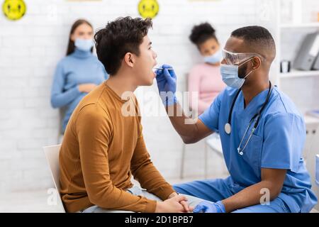 African Doctor Testing Asian Patient for Coronavirus seduta in Clinica Foto Stock