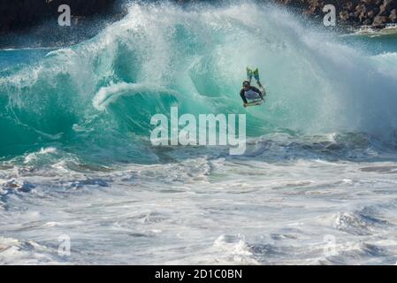 Maui, Hawaii. Giovane uomo su una boogie board che attraversa l'interno di un'onda grande e pericolosa. Foto Stock