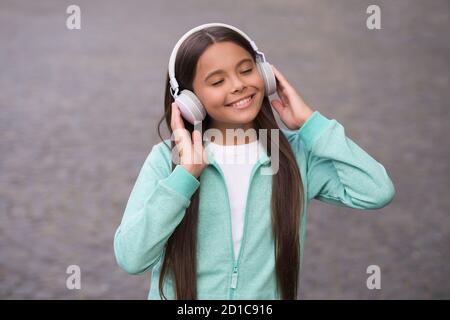 ragazza allegra indossare auricolari con musica canzone all'aperto godendo di melodia, scuola di formazione online. Foto Stock