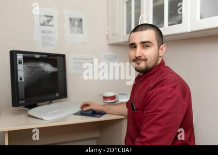 Un medico radiologo sul posto di lavoro guarda le immagini da una macchina a raggi X sul monitor di un computer. Foto Stock