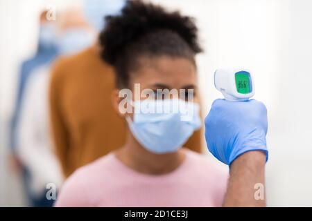Lavoratore medico che esegue lo screening della temperatura per le persone in coda in interni Foto Stock