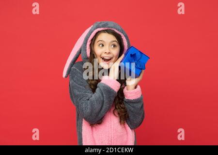 Bell'acquisto. Ragazza teen in pigiami conigliosi. Bambino sorpreso indossare kigurumi coniglio e tenere scatola a sorpresa. Regali e regali. souvenir accessori casa. Sentirsi riposati e felici. Negozio e concetto di shopping. Foto Stock