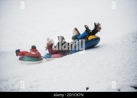 I genitori hanno comprato i loro bambini tubing e ora tutta la famiglia cavalcano giù lo scivolo di ghiaccio. Foto Stock