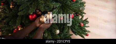 Ampia immagine di una ragazza colorata che tiene in mano due baubles di vacanza dorati e lucenti appesi ad un albero di natale. Foto Stock