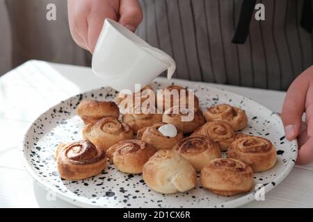 gaffè di cannella a mano umana. fuoco selettivo. involtini di cannella fatti in casa con glassa di crema. concetto di cucina casalinga. primo piano Foto Stock