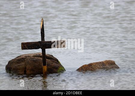Vecchia croce grugnosa di legno appoggiata su una roccia parzialmente coperta d'acqua in un lago Foto Stock
