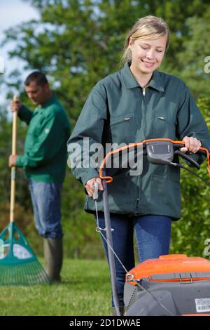 operatrice femminile che utilizza un rasaerba per il taglio di erba verde Foto Stock