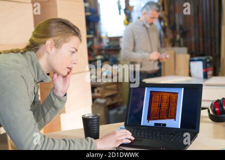 lavoratore femminile che controlla un mobile nello schermo del computer Foto Stock