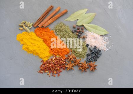 spezie su fondo grigio. composizione festosa composta da cannella, pepe, anice, sale turmerico e rosa. vista dall'alto. spezie asiatiche o condimento orientale. Foto Stock