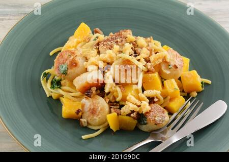 Capesante e piatto di pasta vegetale con kale e zucca di butternut sulla piastra blu con coltello e forcella Foto Stock