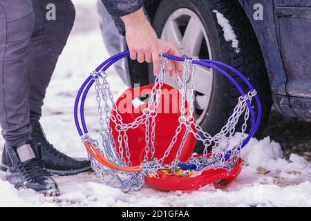 Uomo che anticipa l'auto per viaggiare durante il giorno d'inverno. Catene da neve sulle ruote dell'auto. Foto Stock