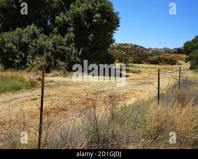 Abbandonata strada sterrata behine un recinto di filo spinato Foto Stock