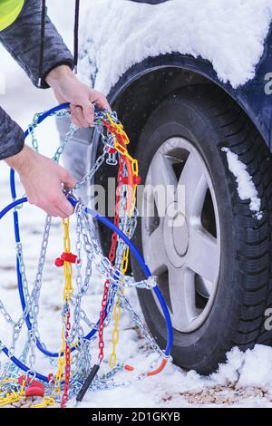 Uomo che anticipa l'auto per viaggiare durante il giorno d'inverno. Catene da neve sulle ruote dell'auto. Foto Stock