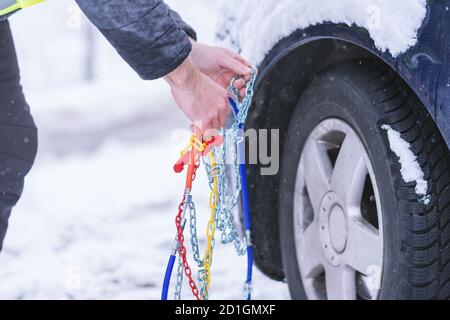 Uomo che anticipa l'auto per viaggiare durante il giorno d'inverno. Catene da neve sulle ruote dell'auto. Foto Stock