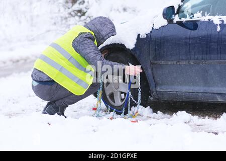 Uomo che anticipa l'auto per viaggiare durante il giorno d'inverno. Catene da neve sulle ruote dell'auto. Foto Stock