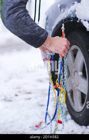 Uomo che anticipa l'auto per viaggiare durante il giorno d'inverno. Catene da neve sulle ruote dell'auto. Foto Stock