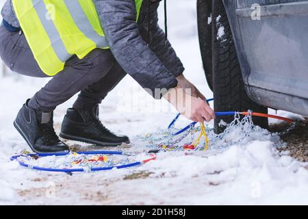 Uomo che anticipa l'auto per viaggiare durante il giorno d'inverno. Catene da neve sulle ruote dell'auto. Foto Stock