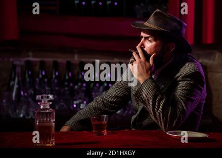 Uomo bearded fumando sigaretta e tenendo un bicchiere di whisky. Foto Stock