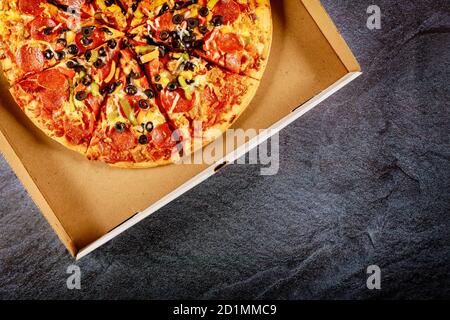 Pizza pepperoni con olive nere in scatola di cartone su fondo scuro. Foto Stock