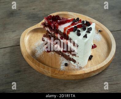 Torta rossa del velluto con frullato di fragola e sciroppo, cibo dolce con cucchiaio e forchetta sul piatto di legno marrone con la tabella in background Foto Stock