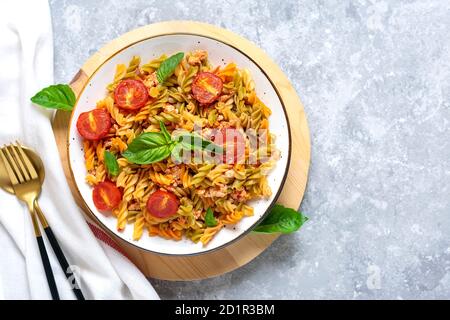 Fusilli - classica pasta italiana di grano duro con carne di pollo, pomodori ciliegia, basilico in salsa di pomodoro in ciotola bianca su tavola grigia in cemento Foto Stock