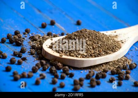 Primo piano di polvere di pepe nero in cucchiaio di legno e di pepe nero su sfondo blu di legno. Fuoco selettivo. Foto Stock