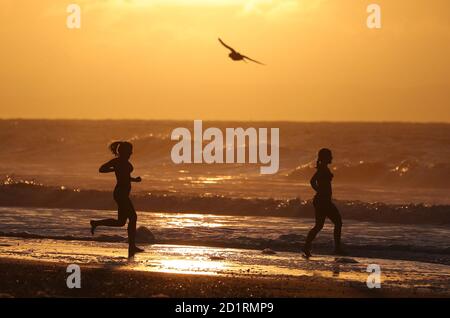 Due nuotatori corrono nel mare mentre il sole sorge sulla spiaggia di Boscombe a Dorset. Foto Stock