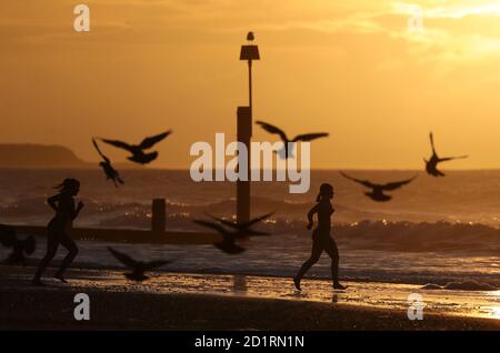 Due nuotatori corrono nel mare mentre il sole sorge sulla spiaggia di Boscombe a Dorset. Foto Stock