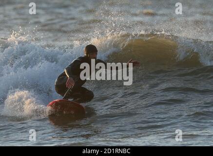 Un surfista corre un'onda nel mare al largo della spiaggia di Boscombe in Dorset. Foto Stock