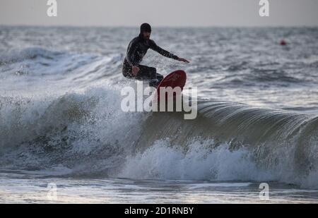 Un surfista corre un'onda nel mare al largo della spiaggia di Boscombe in Dorset. Foto Stock